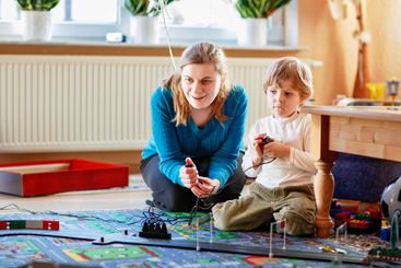 Mother and son playing with racing cars on racetrack,...