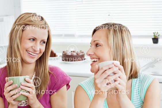 Delighted female friends holding a cup of coffee at home