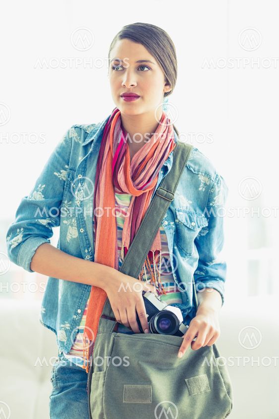Young thinking woman taking camera from her bag