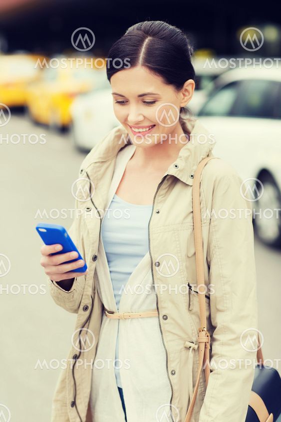 smiling woman with smartphone over taxi in city