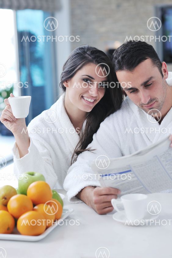 Happy couple reading the newspaper in the kitchen at breakfast