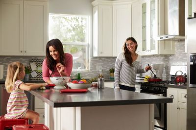 Girl with her female parents, preparing meal in the kitchen