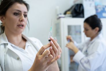 A focused nurse in a white lab coat carefully prepares a...