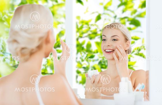 happy woman applying cream to face at bathroom