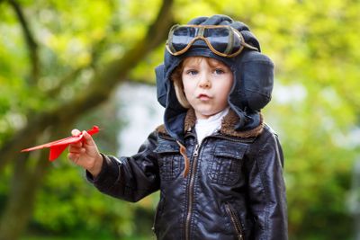 Happy kid boy in pilot helmet playing with toy airplane 