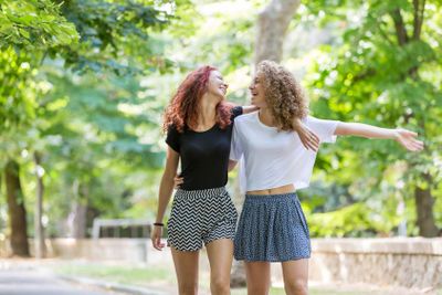 Two girls walking embraced at park. 