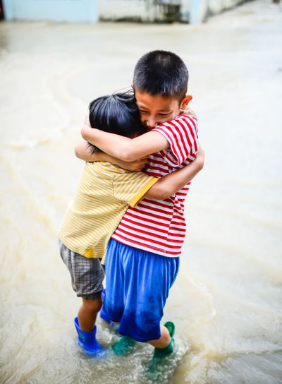 Brother and sister in blue boots holding togetherin flood...