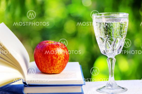Apple on open book and water cup