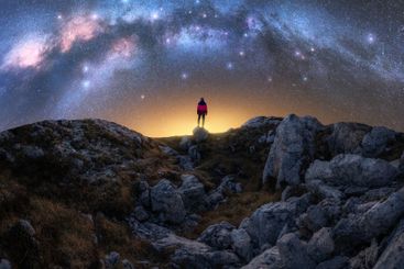 Glowing Milky Way and woman on mountain peak at starry...