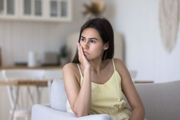 Upset pensive young woman sit on couch with sad look