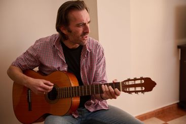 Man playing a classic guitar indoors, expressing...