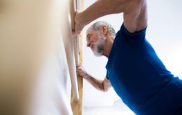 Senior man in gym exercising on wall bars.