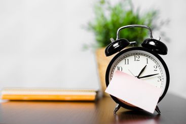 Clock on a desk with a note and a plant in the...