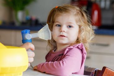 Little toddler girl making inhalation with nebulizer at...
