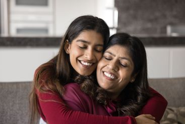 Close up loving Indian daughter cuddling tightly her...