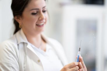 A focused nurse in a white lab coat carefully prepares a...