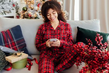 Cute young African woman is sitting on couch and writing...