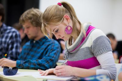 pretty female college student sitting in a classroom full...
