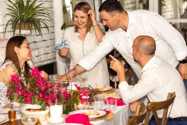 Smiling friends chat and laugh at a festive dinner. Two...