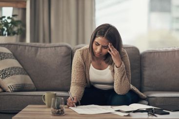 Bills, stress and woman on sofa writing finance notes...