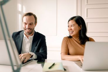 Smiling businesswoman looking at businessman using laptop...
