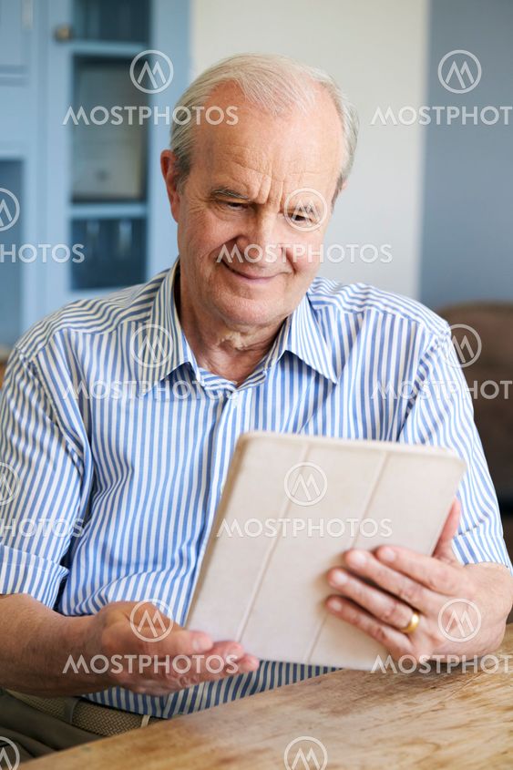 Senior Man Sitting At Home Using Digital Tablet At Table