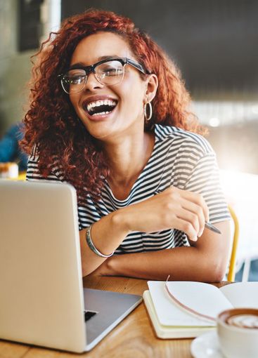 Woman, laptop and notebook with laughing at cafe, smile...