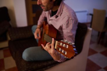 Person playing an acoustic guitar while sitting indoors...