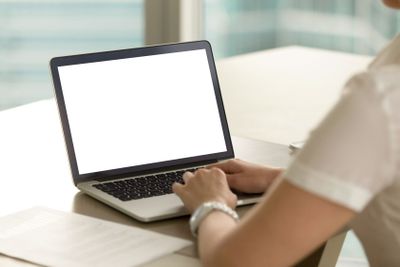 Woman in office working on laptop with mockup blank screen.