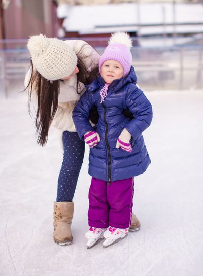 Happy adorable little girl and young mother learning ice-skating