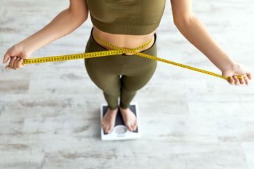 Closeup of Indian woman measuring waist, standing on scales