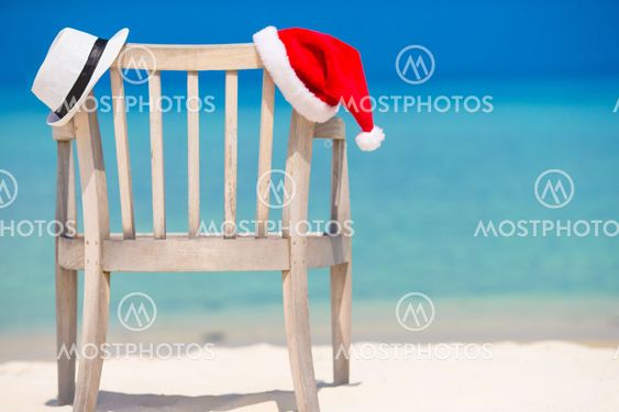 Red santa hat and white straw hat on beach chair at tropical vacation