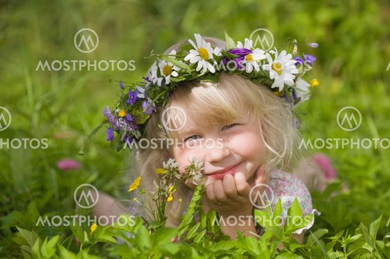 happy little girl in flowers wreath lying on green grass