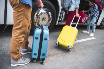 woman putting wheeled bag into travel bus while her...