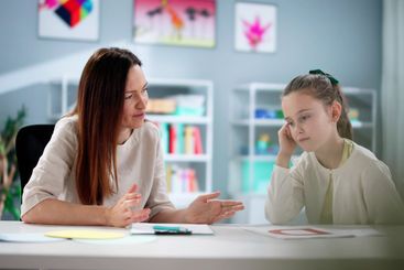 Young woman comforts sad child during counseling session...