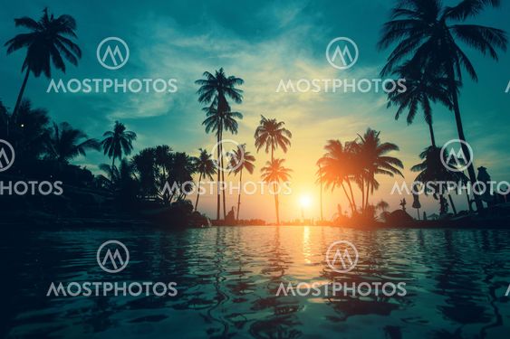 Twilight on a tropical beach with silhouettes of palm trees reflections in water.