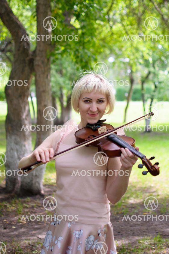 The Russian woman plays a violin in the park in the summer.
