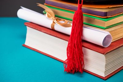 close up of books, diploma and graduation cap with tassel...