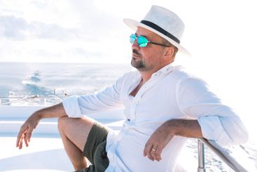 A young man in a white shirt and hat is sitting on board...
