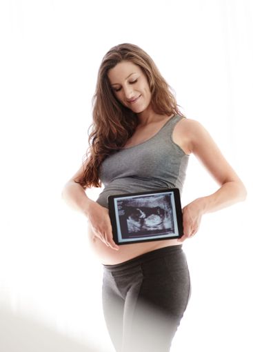 Woman, pregnant and proud with scan on tablet at home...
