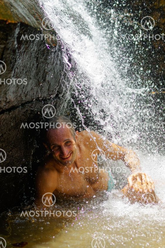 Man taking a relaxing shower under waterfall. outside
