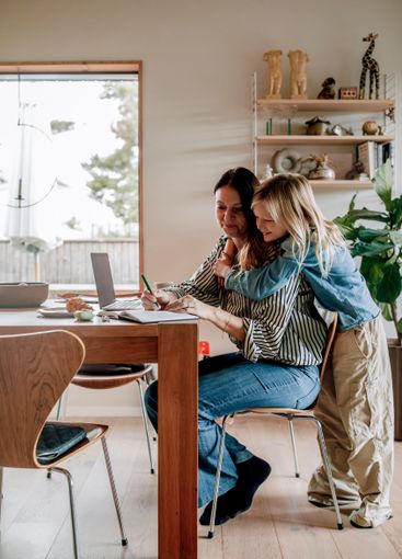 Son embracing mother working while sitting near dining...