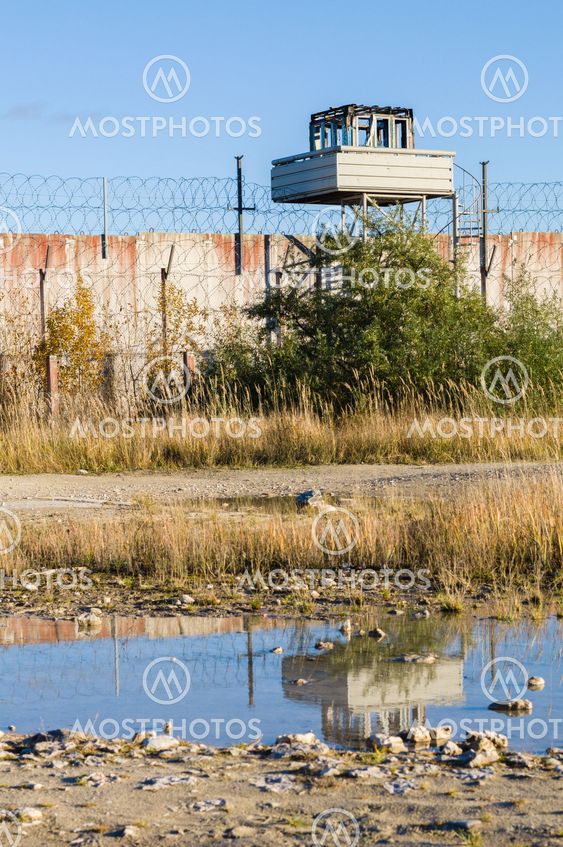 Abandoned watch-tower and prison wall with reflection in puddle