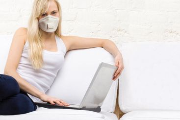 Happy woman in protective mask using laptop at home