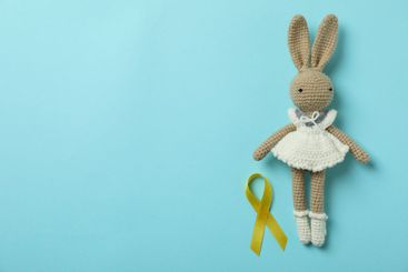 Toy bunny and childhood cancer awareness ribbon on blue...