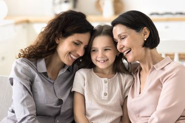Happy smiling little girl sit on couch between mom grandma