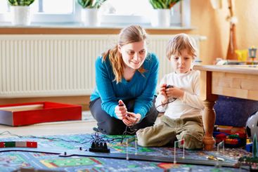 Mother and son playing with racing cars on racetrack,...