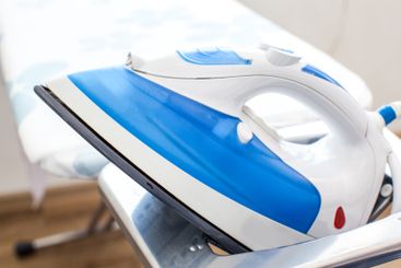 Iron on ironing board on light home interior background