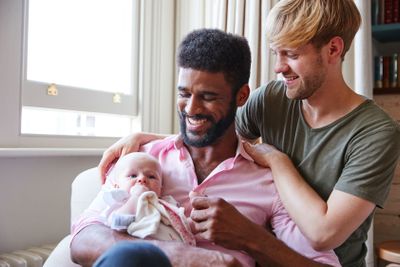 Loving Male Same Sex Couple Cuddling Baby Daughter On...