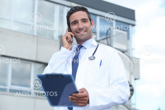 Male doctor outside hospital making phone call